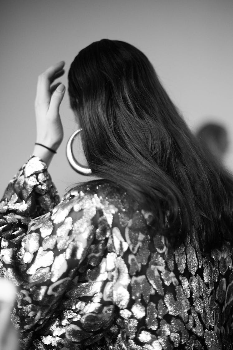 A woman wearing a silver sequin blazer and silver round earrings