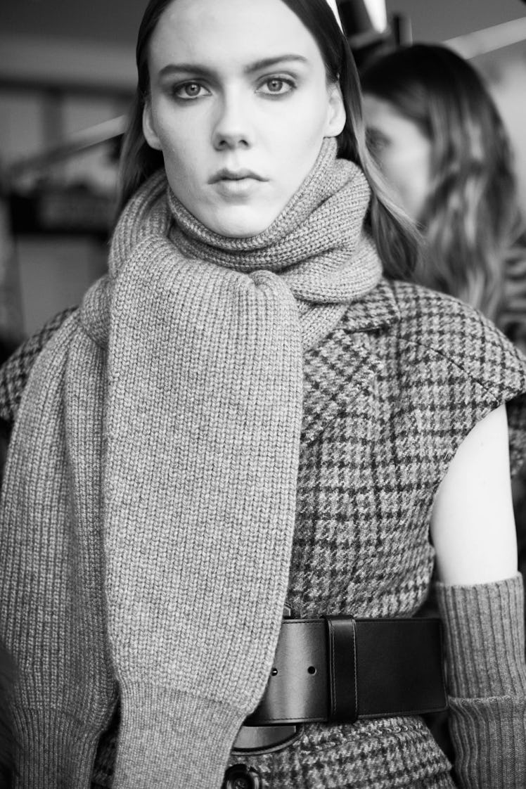A female model wearing a wide and long grey woolen scarf and a plaid dress with a black belt