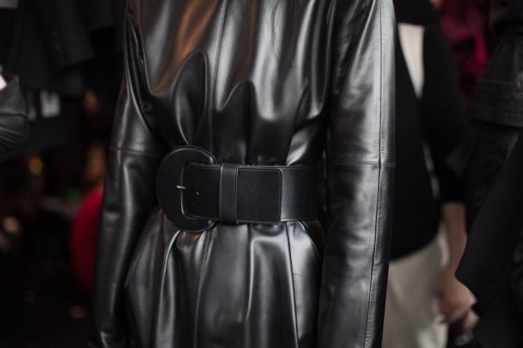 A model standing in a silver dress with a black belt