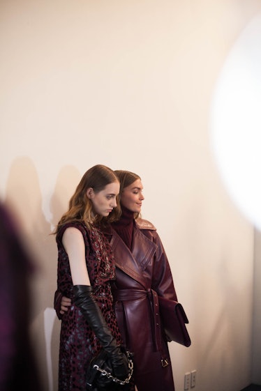 A woman in a purple coat and sweater combination posing for a photo with a woman that is wearing a p...