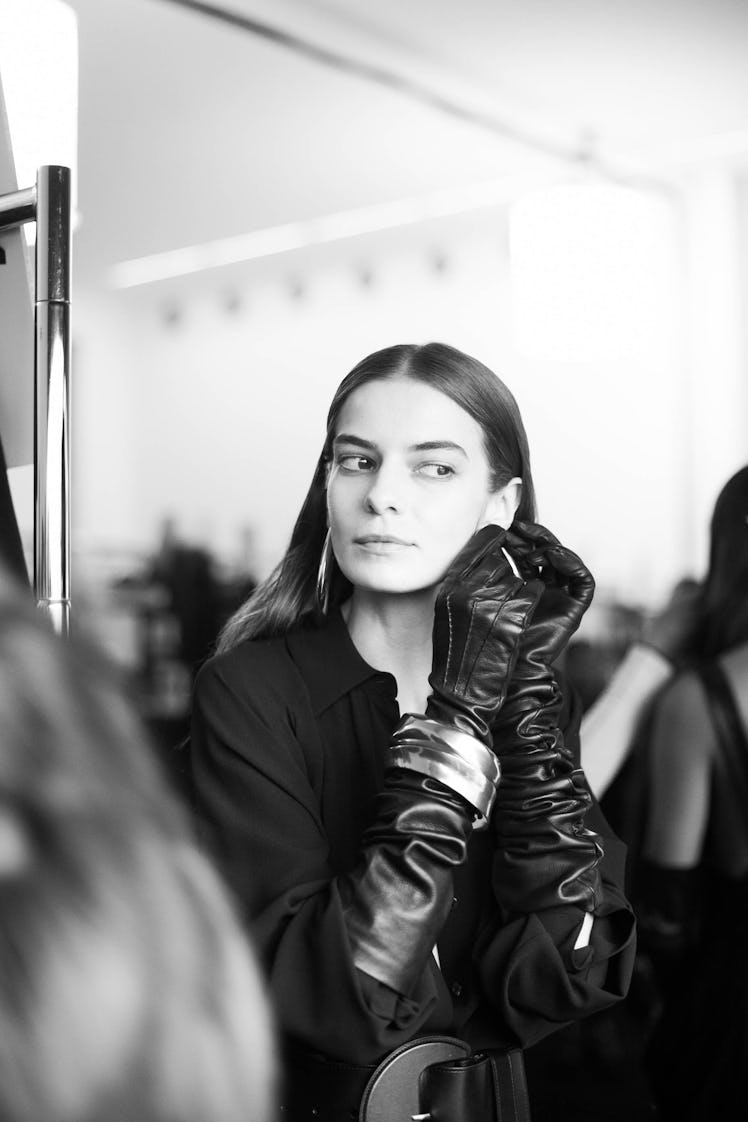 A female model putting round earrings on her ears while wearing black gloves 