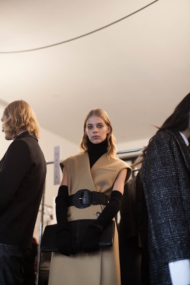 A blonde female model posing while wearing a light brown coat with a black belt