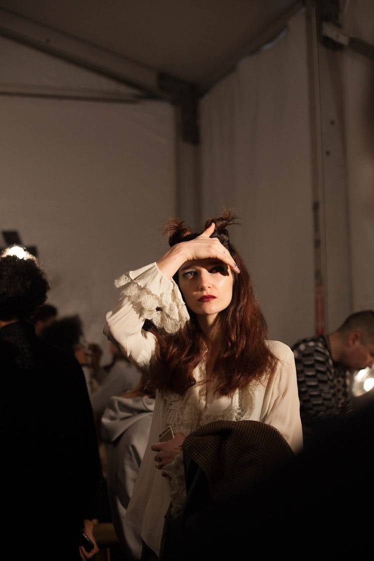A model in a white blouse and a double top knot with her hand over her face backstage at Anna Sui Fa...