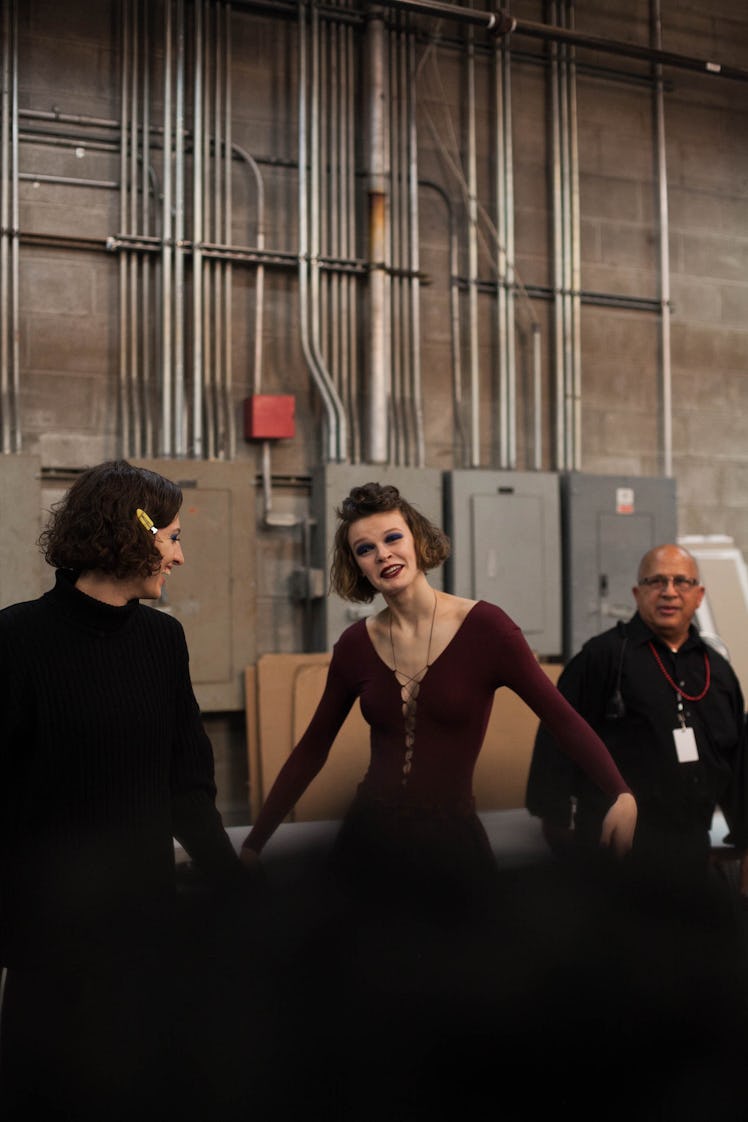 A model in a black dress and a model in a burgundy dress posing and smiling backstage at Anna Sui Fa...