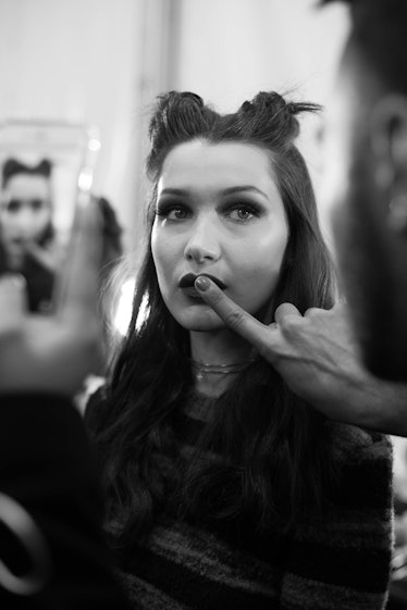 Bella Hadid with a double knot getting her lipstick applied by a makeup artist backstage at Anna Sui...
