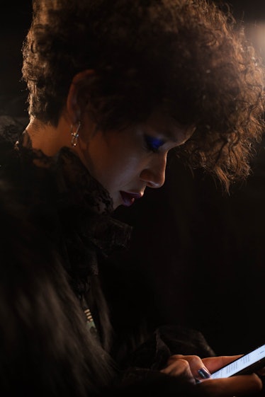 A brunette model with curly hair in a black coat looking at her smartphone backstage at Anna Sui Fal...