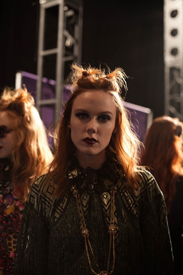 A portrait of a model in a black-gold dress with a double top knot backstage at Anna Sui Fall 2017
