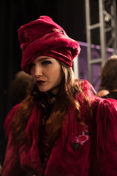 A model in a red coat and a red hat  backstage at Anna Sui Fall 2017