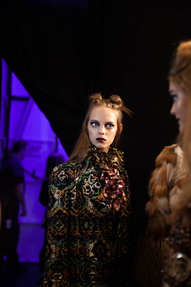 A model in a black green orange shimmer coat and scarf and a double knot backstage at Anna Sui Fall ...