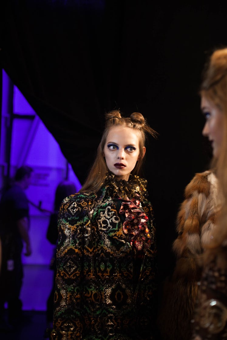 A model in a black green orange shimmer coat and scarf and a double knot backstage at Anna Sui Fall ...