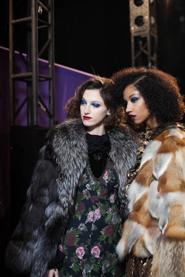 A model in a green floral dress and grey coat and a model in a brown coat backstage at Anna Sui Fall...