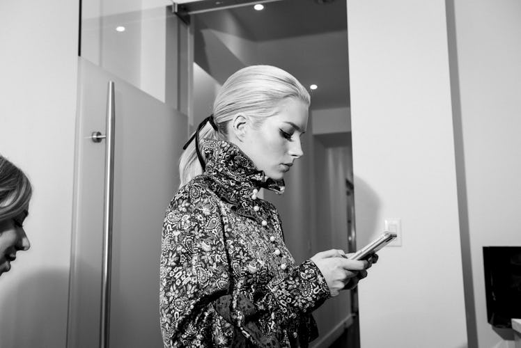 Lottie Moss typing on her phone while wearing a silver coat