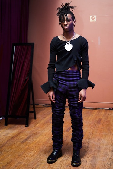 A male model posing with a silver Vaquera & Co chain necklace while wearing a black shirt and blue p...