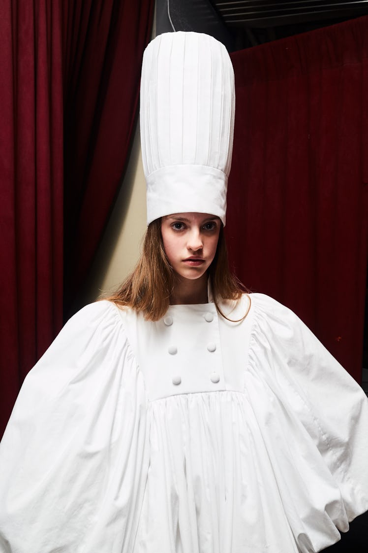 A female model posing in a white cook uniform shaped dress and cap