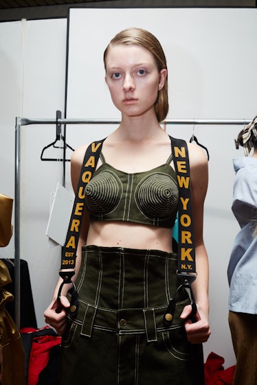 A female model posing while wearing a green top and black trousers