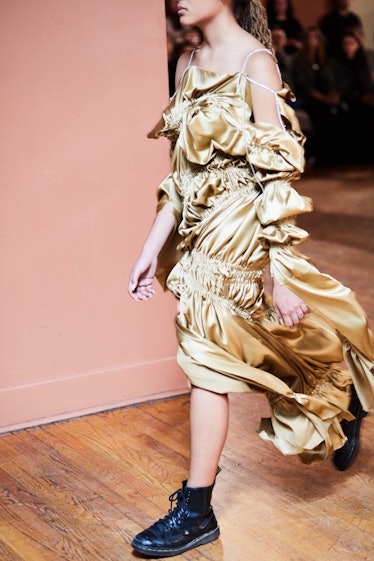 A female model walking while wearing a golden gown and black boots