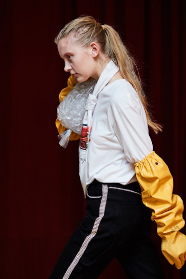 A female model walking and carrying a big ice bag while wearing a white shirt and yellow gloves