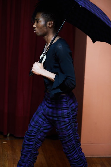 A model walking with a black and blue plaid umbrella while wearing a black shirt and black and blue ...