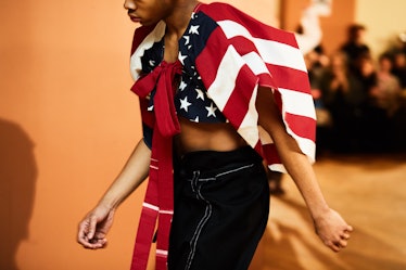 A model walking while wearing black pants and a blazer with a drawing of the American flag 