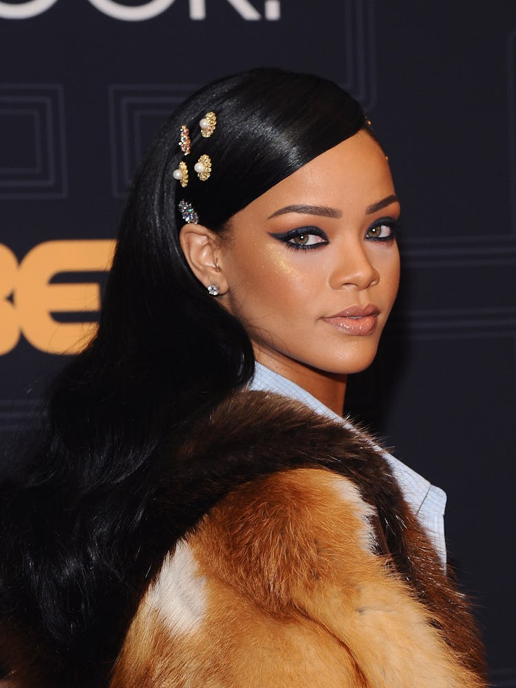 Rihanna wearing a fur coat, slicked back hair with pearl hair clips and a bold cat eye 