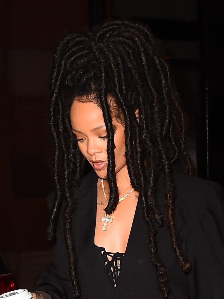 Rihanna with long black dreadlocks, in a black dress and a large diamond cross walking around Soho