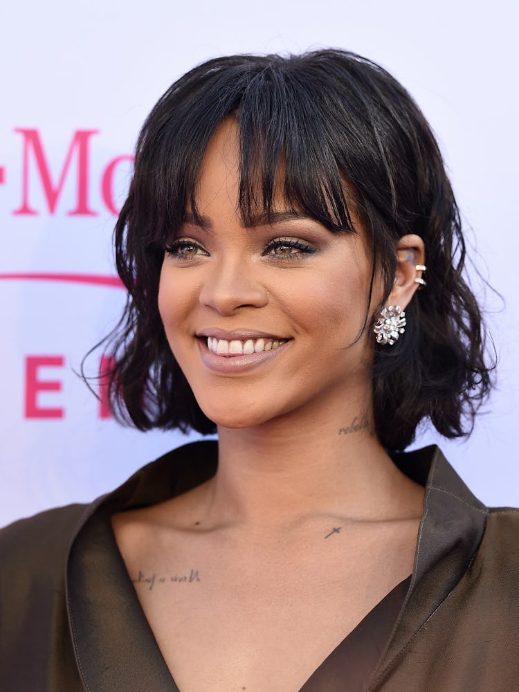 Rihanna with a short curly bob and bangs, black eyeliner and grey eyeshadow smiling at the Billboard...