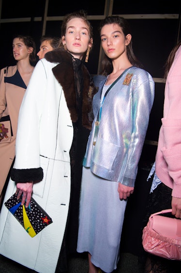 A model in a white coat with brown fur collar and a model in a blue sweater and skirt at the Christo...