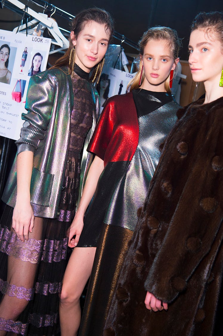 A model in a brown coat and two models in grey-green metallic dresses at the Christopher Kane Fall 2...