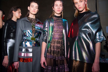 Three models in a coat and dresses in metallic grey with red and blue sequin accents at the Christop...