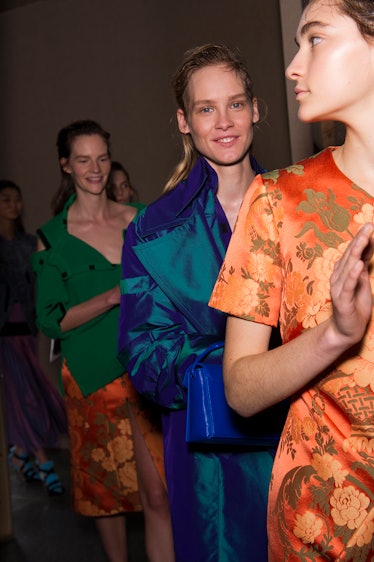A model in a green top and orange skirt, a model in a blue dress and a model in an orange floral dre...