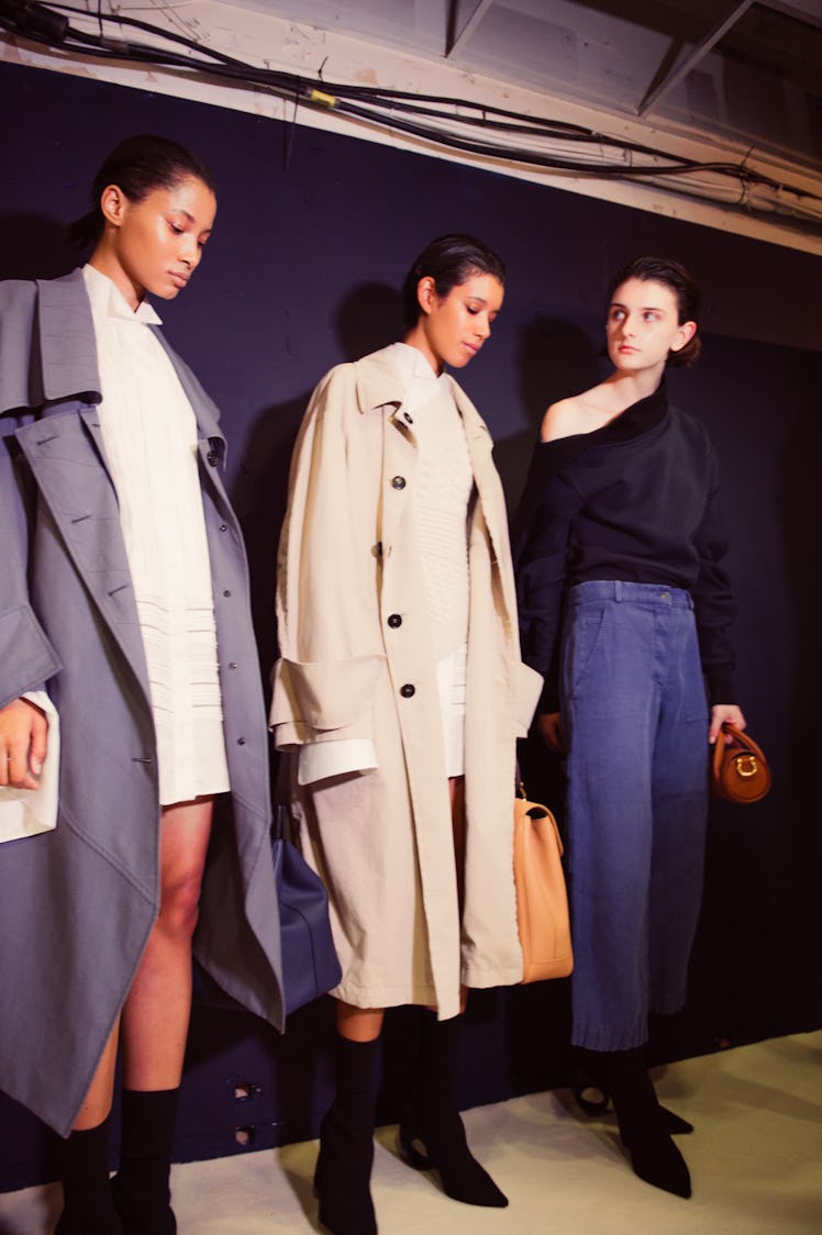 Two models posing in light brown and light blue coats and one model posing in a black shirt