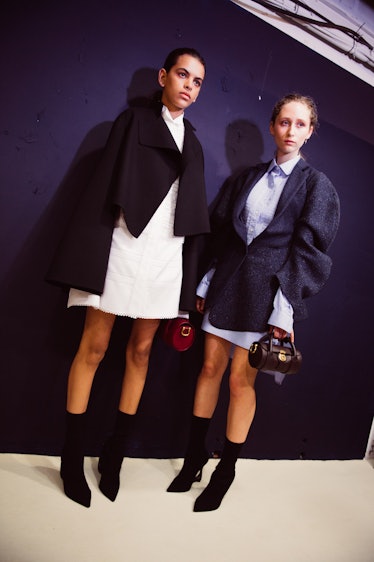 Two female models posing while wearing black blazers over white and light blue mini dresses