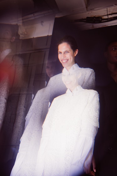 A black-haired female model smiling while posing or a photo in a white dress