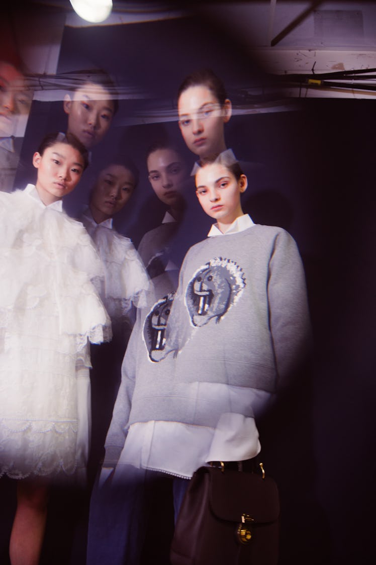 Blurred two women posing while wearing white dresses and grey sweaters over white shirts