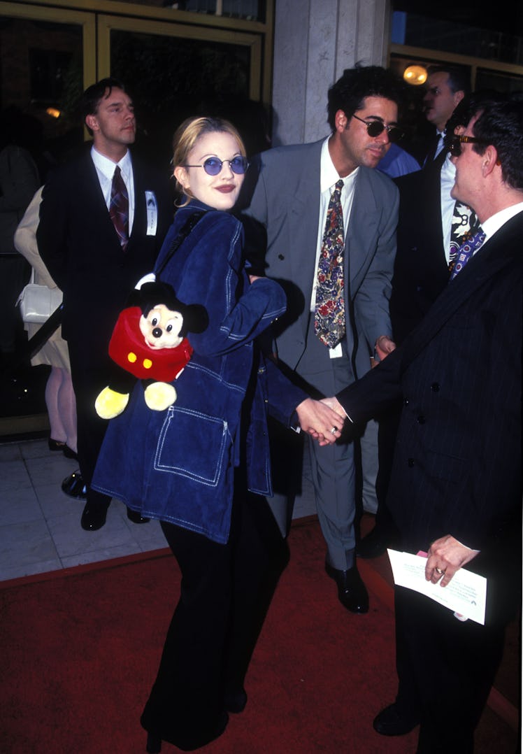Drew Barrymore wearing blue-tinted sunglasses with an oversized blue jean jacket and a Mickey Mouse ...