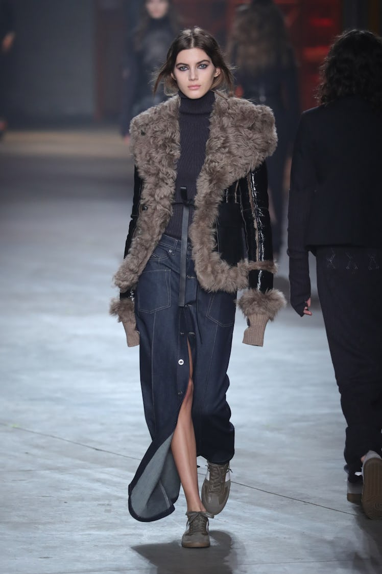 A female model walking in a Diesel Black Gold elongated silhouette like denim maxi skirt paired with...
