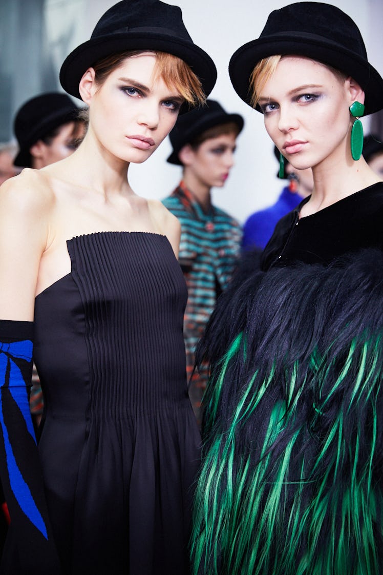 Two female models posing in black dresses while wearing black bucket hats 