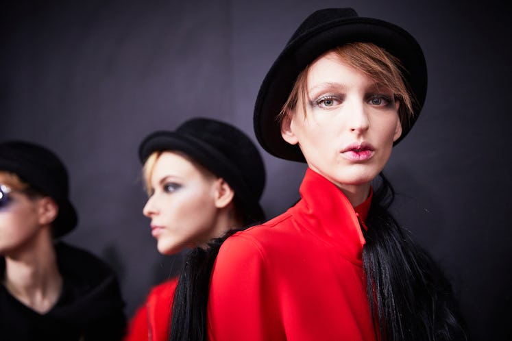 Two female models dressed in red coats that are paired with black hats