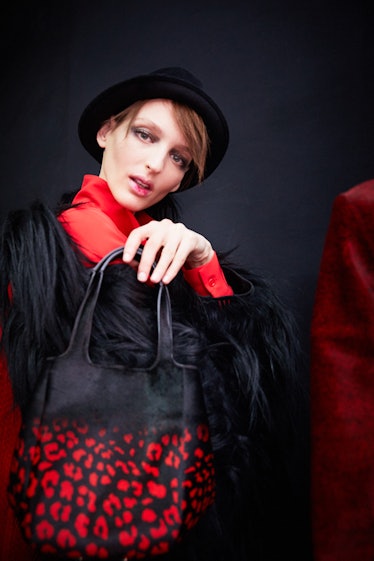 A female model with a black hat holding a red and black handbag