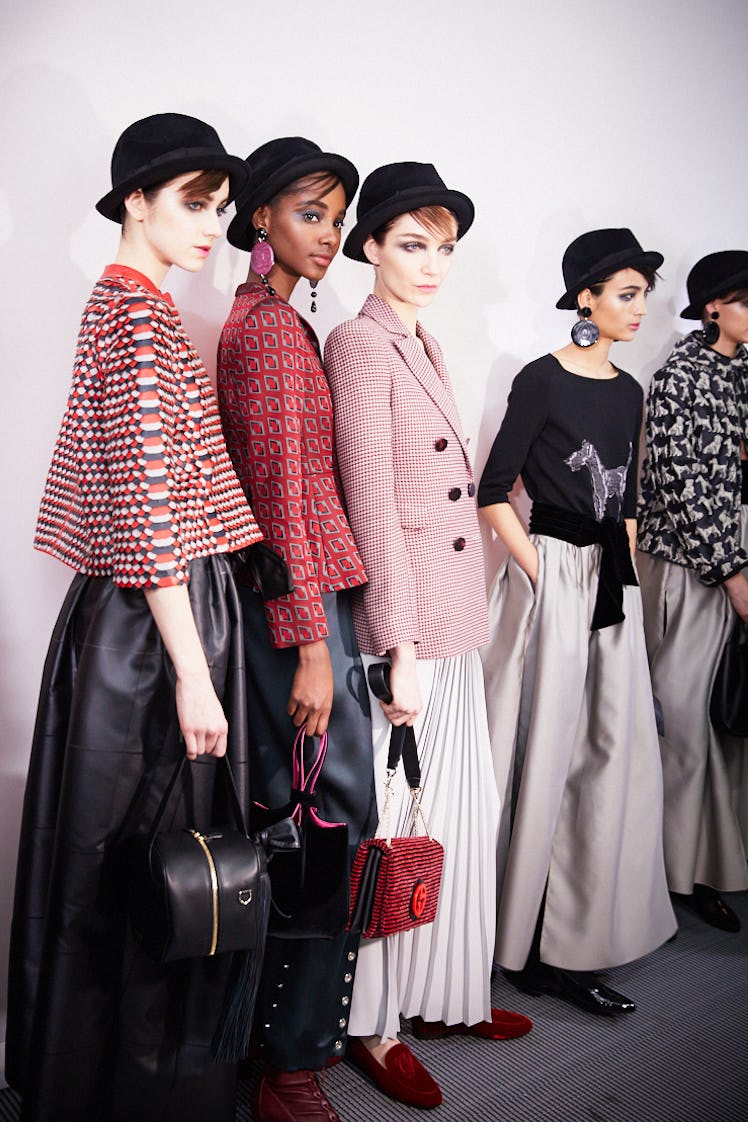 Five female models posing for a photo while wearing black hats