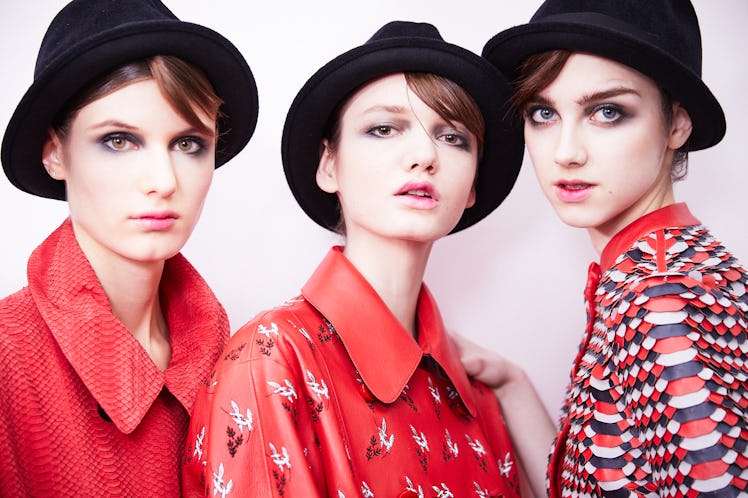 Three female models posing for a photo in red shirts and black bucket hats 