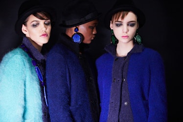 Three models posing in blue coats paired with black hats 