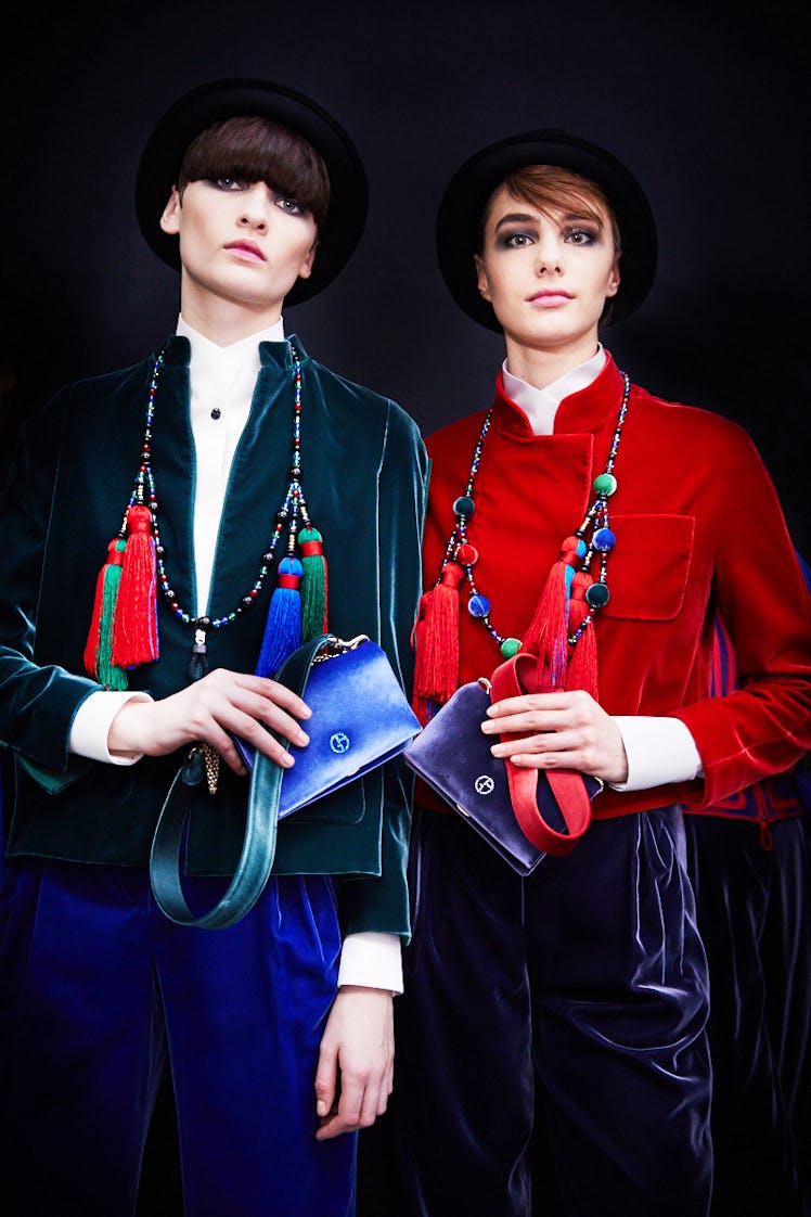 Two models posing in red and green blazers paired with black hats and purple and blue bags