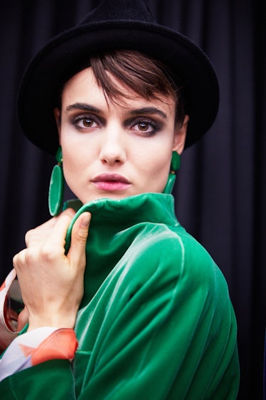 A woman posing for a photo while wearing a green coat and black hat