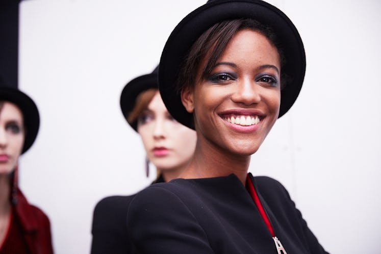 A young lady smiling while posing for a photo in a black blazer and black hat