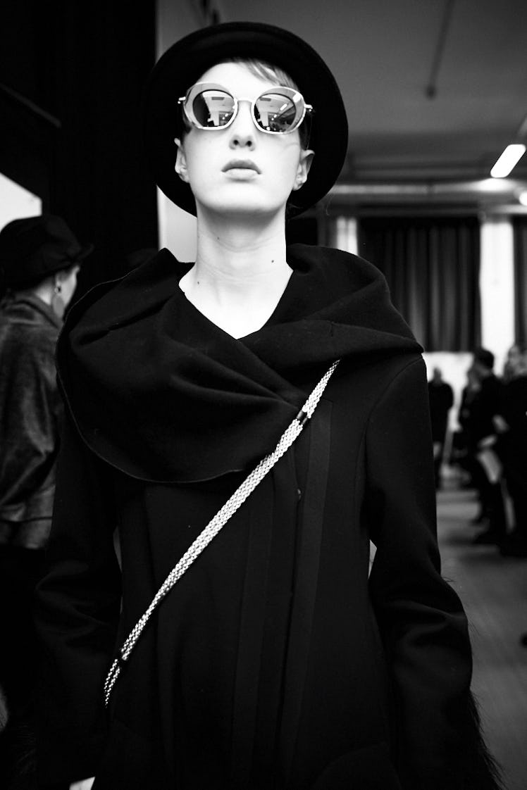 A female model walking in a black dress, a black hat, and with sunglasses on her head 