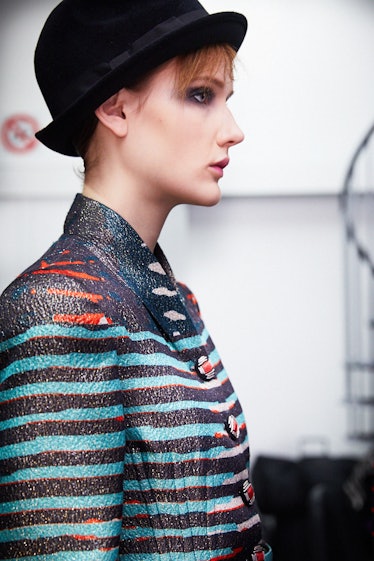 A female model walking in a blue and black blazer while wearing a black hat on her head 