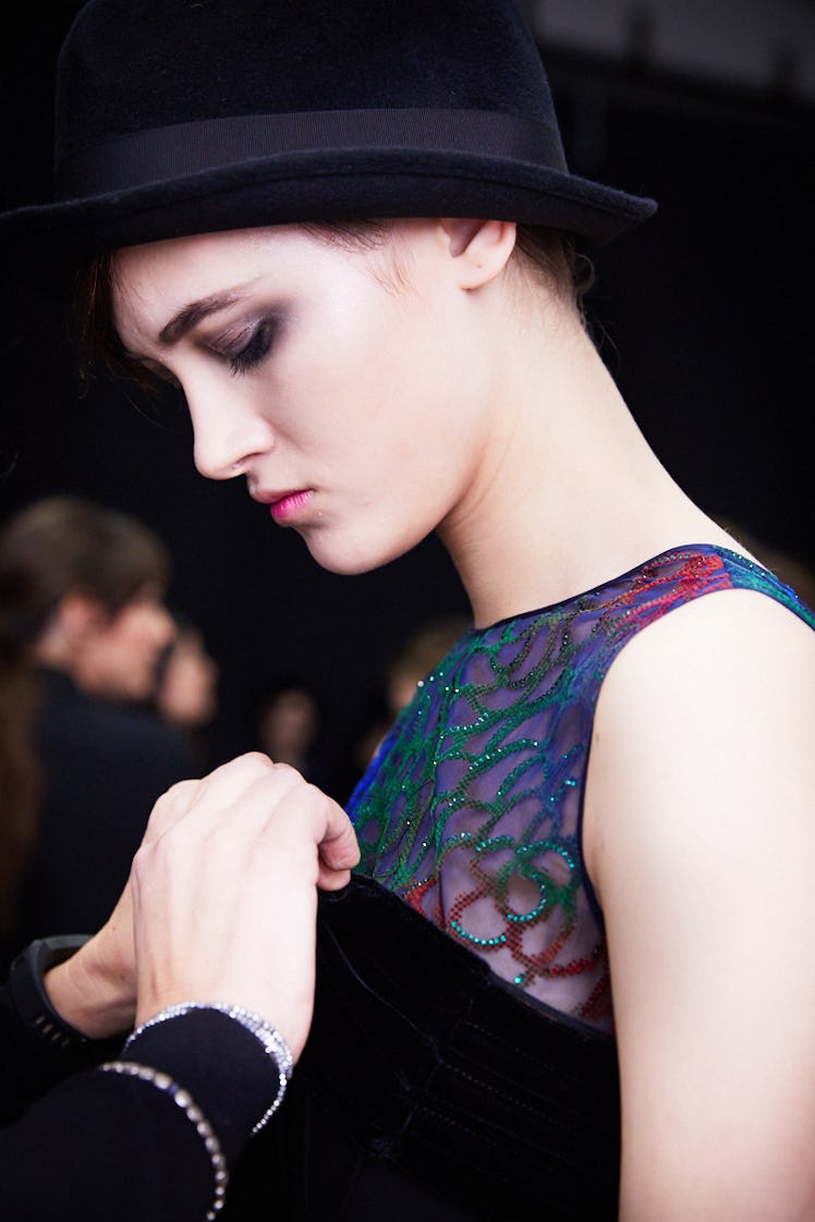 A female model with a black hat watching a designer putting a dress on her 