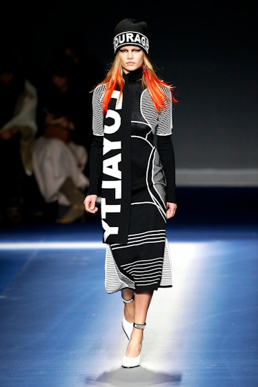A female model walking in a black Versace dress with an "equality" text sign