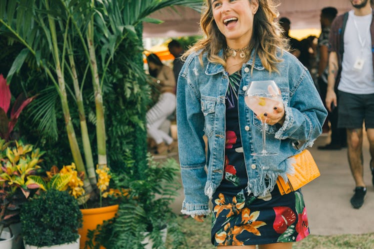 A woman in a floral dress and a denim jacket, holding her drink at Veuve Clicquot’s Third Annual Car...